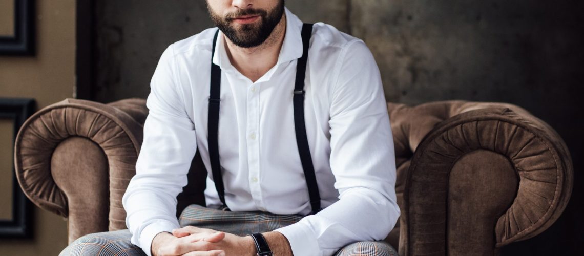 fashionable man in glasses and suspenders sitting in armchair